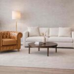 Sala d’attesa moderna con poltrona Chesterfield pelle cuoio, divano bianco, tavolino centrale e lampade da terra beige.