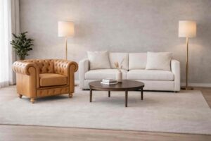 Sala d’attesa moderna con poltrona Chesterfield pelle cuoio, divano bianco, tavolino centrale e lampade da terra beige.
